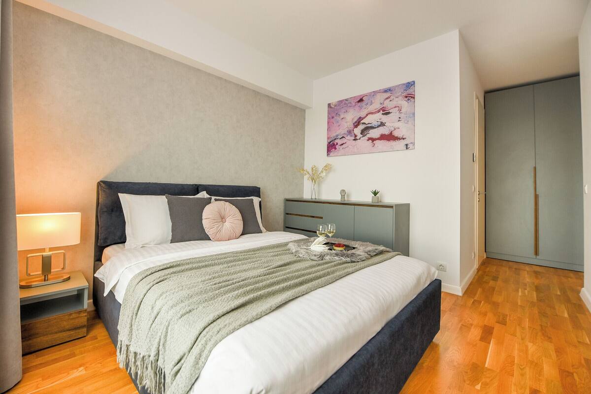 A bedroom with a bed, bedside table, lamp, artwork, and a wardrobe.