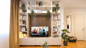 Uma sala de estar com televisão, prateleiras com plantas e uma porta.