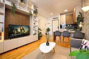 A modern living room with a flat-screen TV, a white coffee table, and a dining area with chairs. - Modern Apartments near Romexpo (Bucharest)