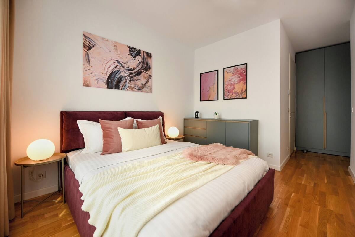 A bedroom with a large bed, bedside lamps, a dresser, and artwork on the wall.