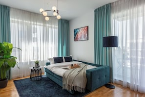 A bedroom with a bed, curtains, a plant, a lamp, and a painting. - Modern Apartments near Romexpo (Bucharest)