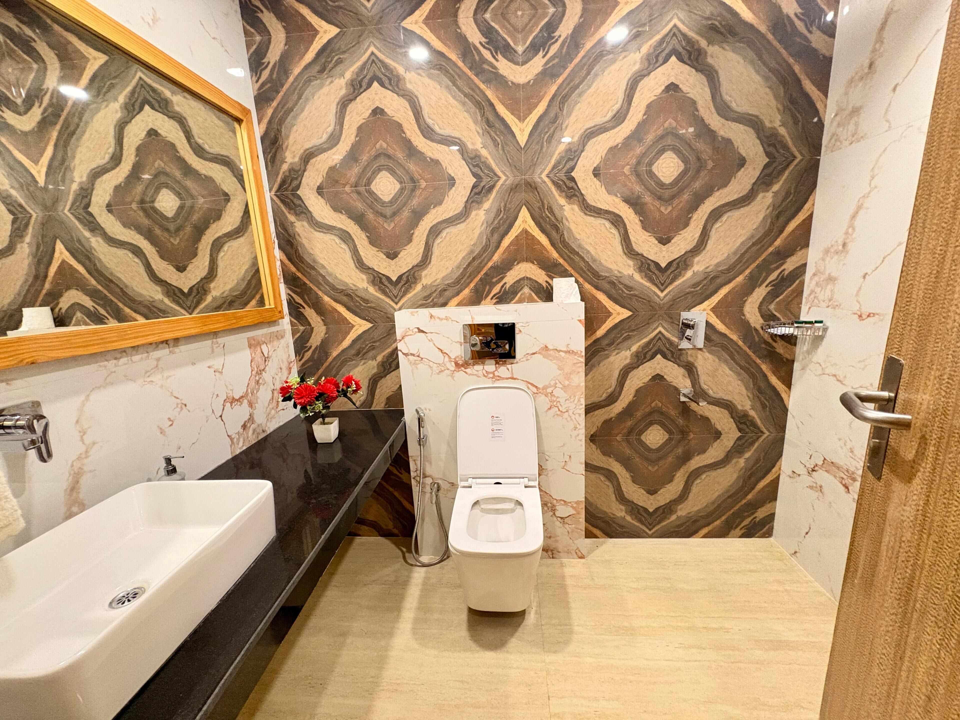A modern bathroom with a marble-patterned wall, a black countertop, a white sink, and a toilet.