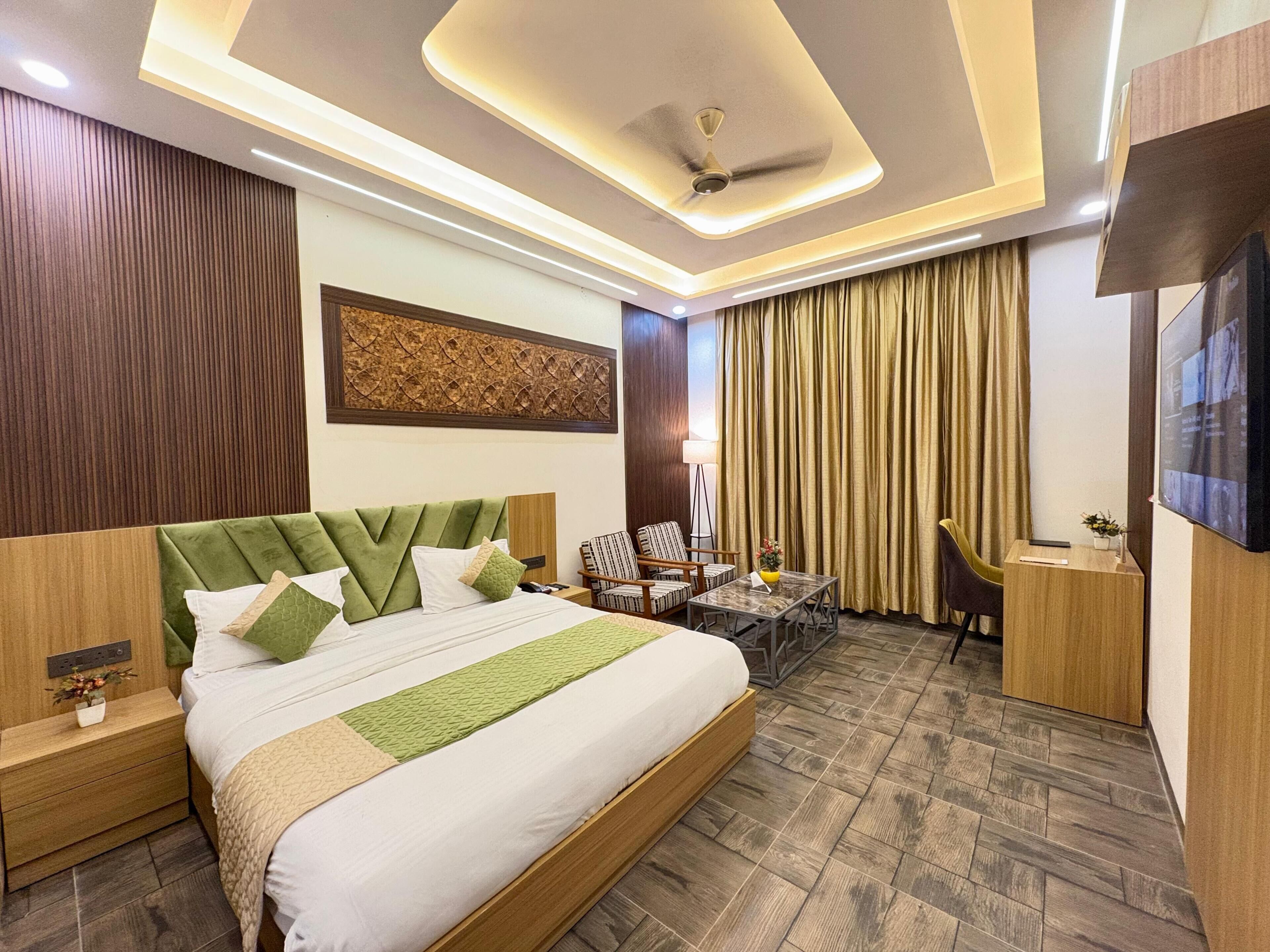 A hotel room with a large bed, a desk, a chair, a TV, and a ceiling fan.