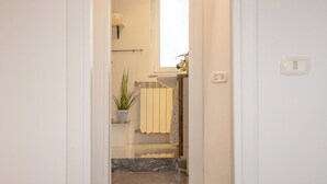 A hotel room with a bed, a bathroom visible through an open door, and a potted plant. - Petito House - Cozy apartment surrounded by greenery. (Giugliano in Campania)