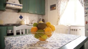 A kitchen with teal cabinets, a white stove, and a fruit bowl on a table with a floral tablecloth. - Petito House - Cozy apartment surrounded by greenery. (Giugliano in Campania)