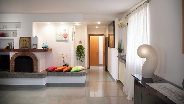 A modern living room with a fireplace, a hallway leading to a door, and a dining area with a table and chairs. - Petito House - Cozy apartment surrounded by greenery. (Giugliano in Campania)