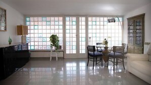 A spacious living room with a dining area, large windows with frosted glass, a white sofa, and a plant. - Petito House - Cozy apartment surrounded by greenery. (Giugliano in Campania)