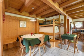 Ein Holzinnenraum mit Esstisch, Stühlen, einem Stockbett und einer kleinen Küche.