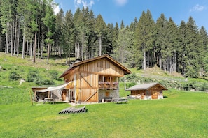Una cabaña de madera con base de piedra, un balcón con flores y una mesa de picnic en un área boscosa.