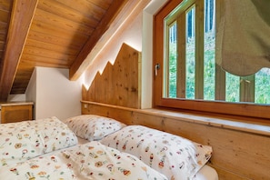 Ein Schlafzimmer mit Holzbalkendecke, einem Fenster mit Blick auf Grünflächen und floralem Bettzeug.