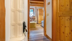 A hallway with wooden flooring, a wooden door, and a room with a bed and a window.