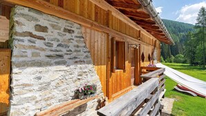 A wooden cabin with a stone wall, wooden porch, and a ski slope in the background.