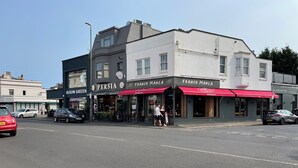 Straatbeeld met restaurants Persia en Franco Manca, een riooldeksel en geparkeerde auto's.