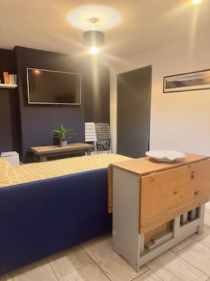Una habitación moderna con sofá, una mesita con una planta, televisor en la pared y un armario de madera.
