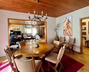 A dining area with a round table, chairs, a chandelier, and a large painting on the wall.