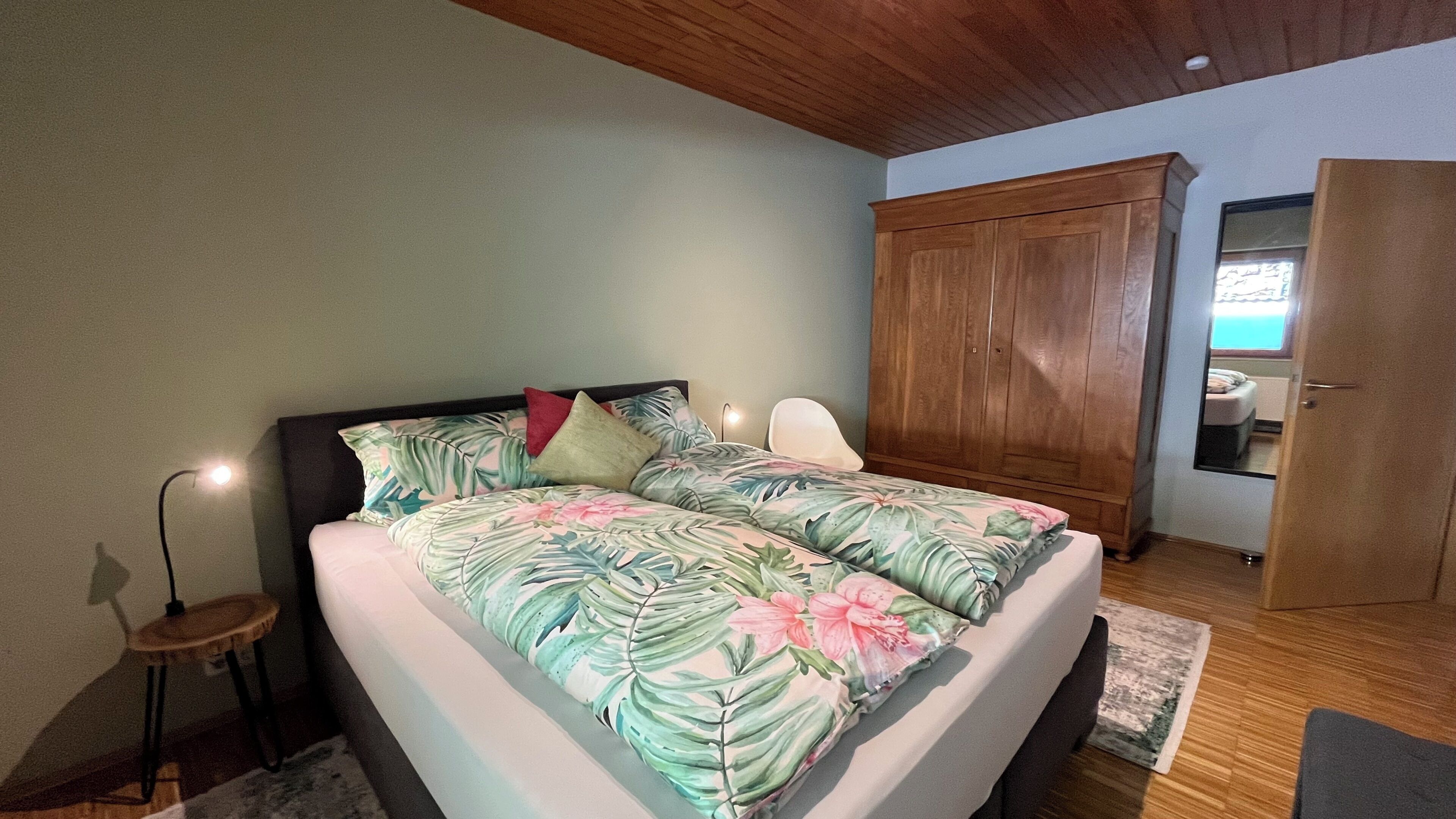 A bedroom with a bed, a wardrobe, a bedside lamp, and a small table.