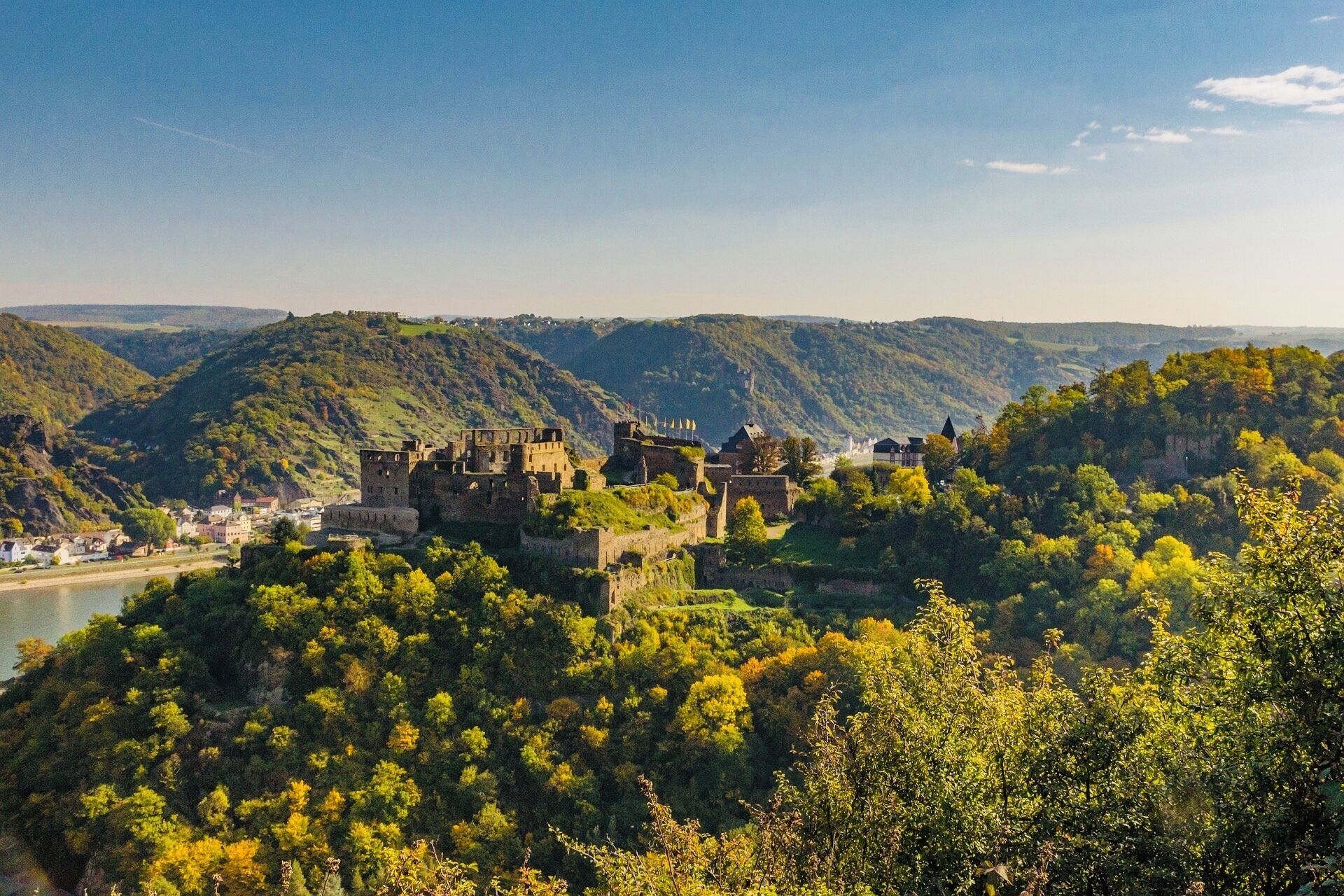 Un castillo histórico en una colina con vistas a un río, rodeado de abundante vegetación.