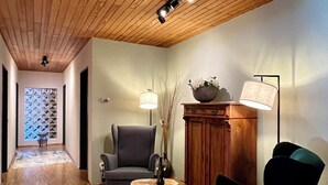 A hallway with wooden flooring, a grey armchair, a green armchair, a wooden cabinet, and a floor lamp.