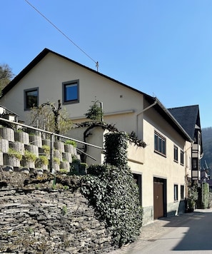 A two-story building with a stone wall and a large hedge in front.