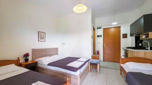 Ein Hotelzimmer mit zwei Betten, einem kleinen Schreibtisch, einem Stuhl, einer Küchenzeile und einer Tür zu einem weiteren Raum.