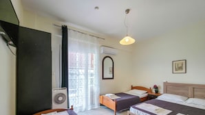 Ein Hotelzimmer mit zwei Betten, einem Fenster mit Vorhängen, einem Deckenventilator und einer Wand-Klimaanlage.