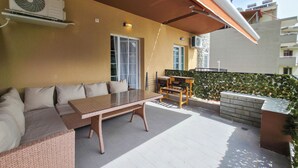 Ein Balkon mit einer Rattan-Couch, einem Glastisch und einem kleinen Holztisch.