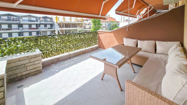 Ein Balkon mit Tisch, einem Rattangeflechtsessel und Blick auf Gebäude.