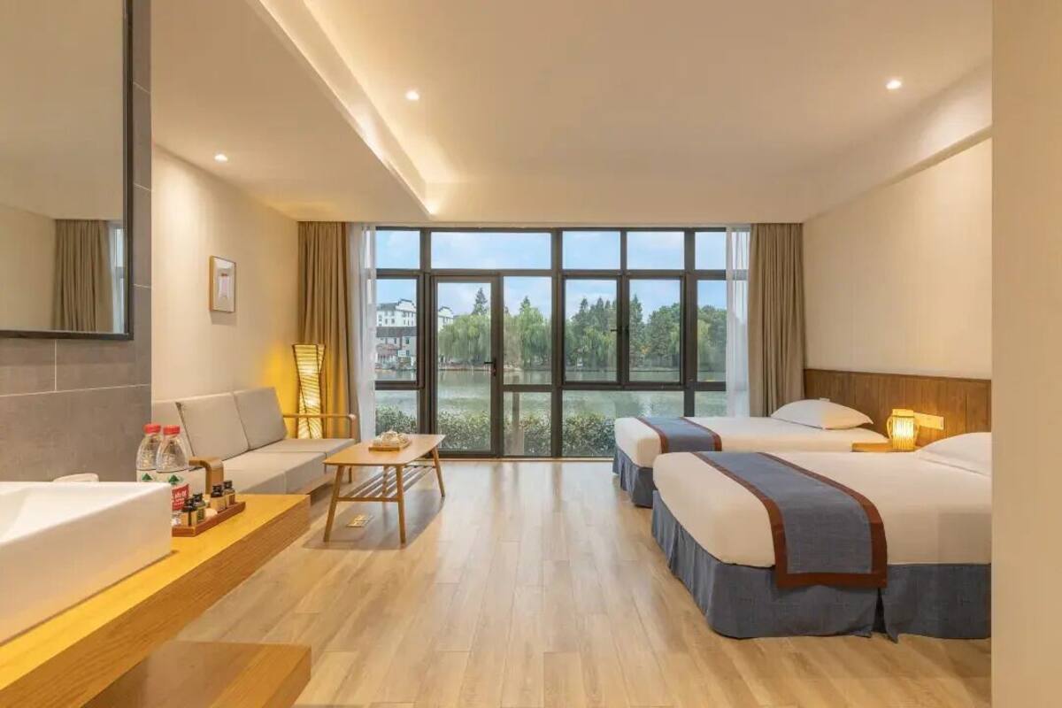 Habitación de hotel con sofá, una mesita, escritorio, dos camas y un ventanal con vistas a zonas verdes.