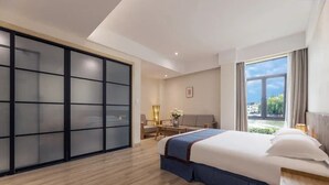 A modern hotel room with a large bed, a sliding door closet, a desk with a chair, and a view of the outdoors.