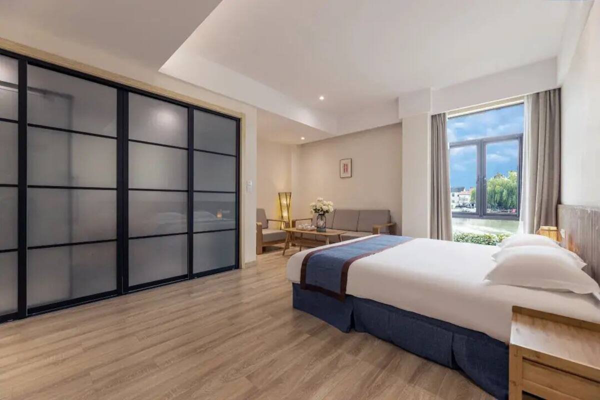 Una habitación de hotel moderna con una cama grande, un armario con puerta corredera, un escritorio con silla y vistas al exterior.