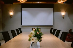 Une salle de conférence avec une longue table, des chaises noires, un arrangement floral au centre et un écran de projection.