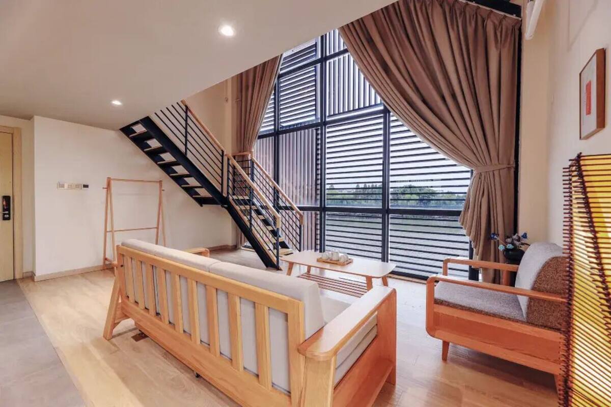 Un interior moderno con un banco de madera, un sofá, una escalera y ventanas grandes.