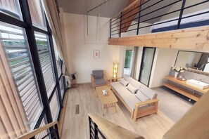 A modern living room with a sofa, coffee table, and a chair. There is a wooden staircase leading to an upper level. - Lake Villa Boutique Guesthouse (Shanghai)