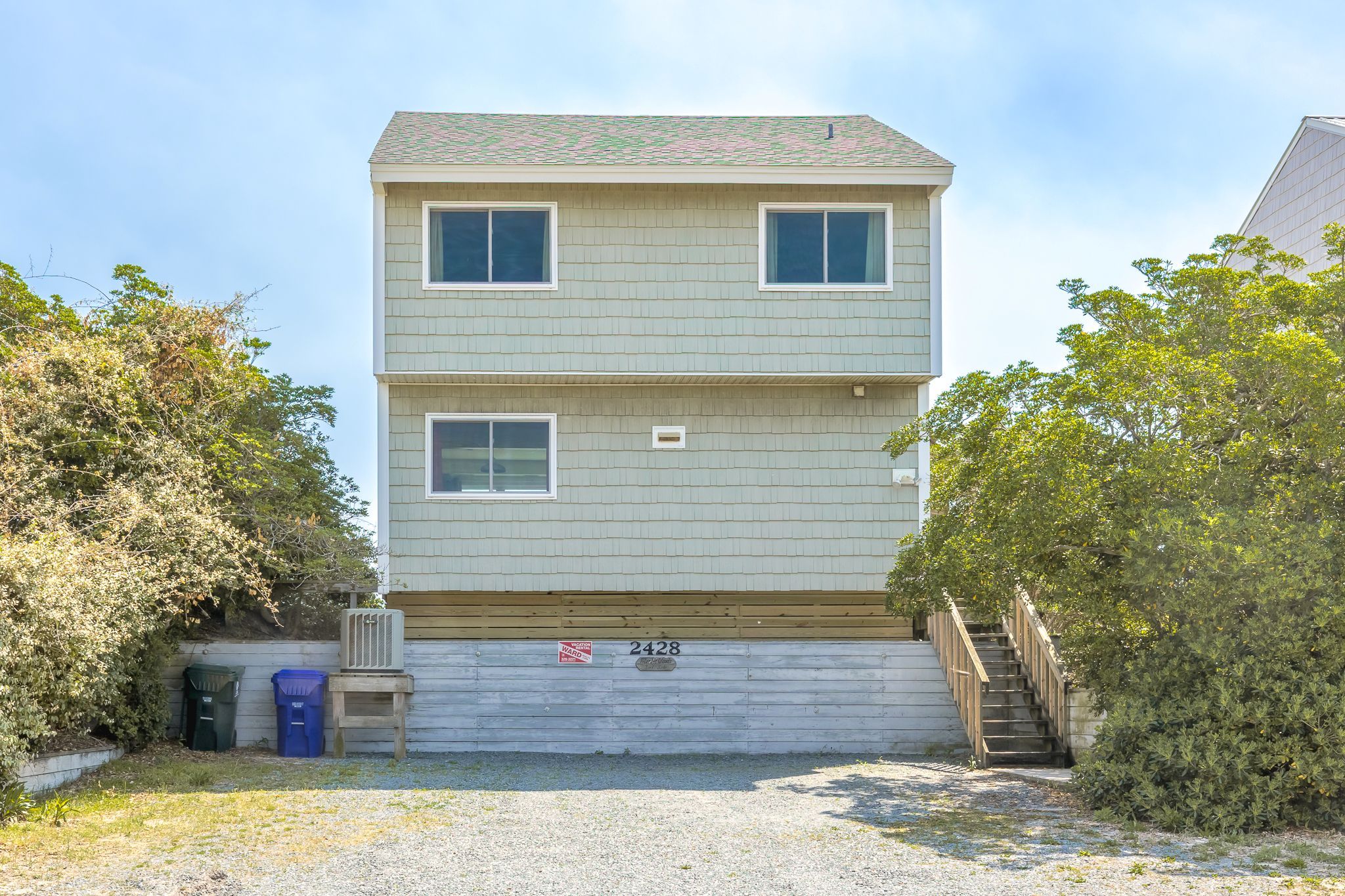 A two-story building with a flat roof, a front entrance with a wooden staircase, and a small porch area.