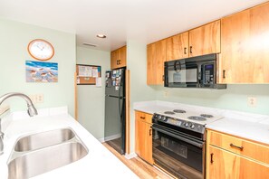 A kitchen with a stainless steel sink, wooden cabinets, a black refrigerator, a microwave, and a stove. - Marble Winds with a large, oceanfront sundeck with impressive views and built-in (Surf City)