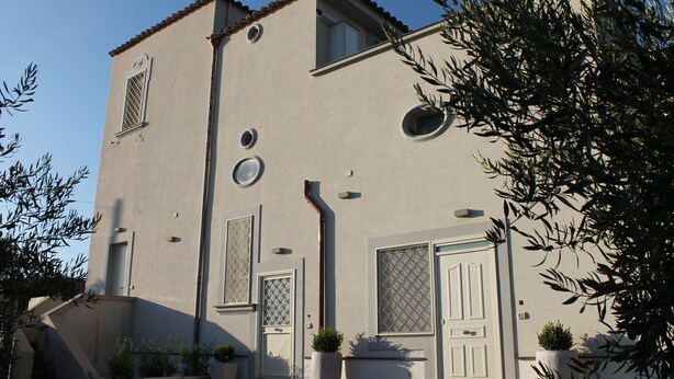A building with a symmetrical facade, multiple windows, and doors, surrounded by potted plants.