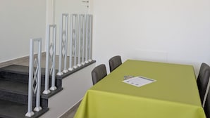 A conference room with a green table, four chairs, a white door, a staircase with white railings, and a wall-mounted air conditioner.
