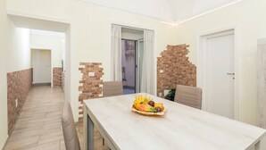 Een eetgedeelte met een tafel gedekt met fruit, een accentmuur van baksteen en een deur naar een andere kamer.