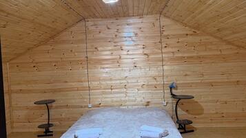 A wooden room with a bed, two small tables, a hanging light fixture, and a door with keys.