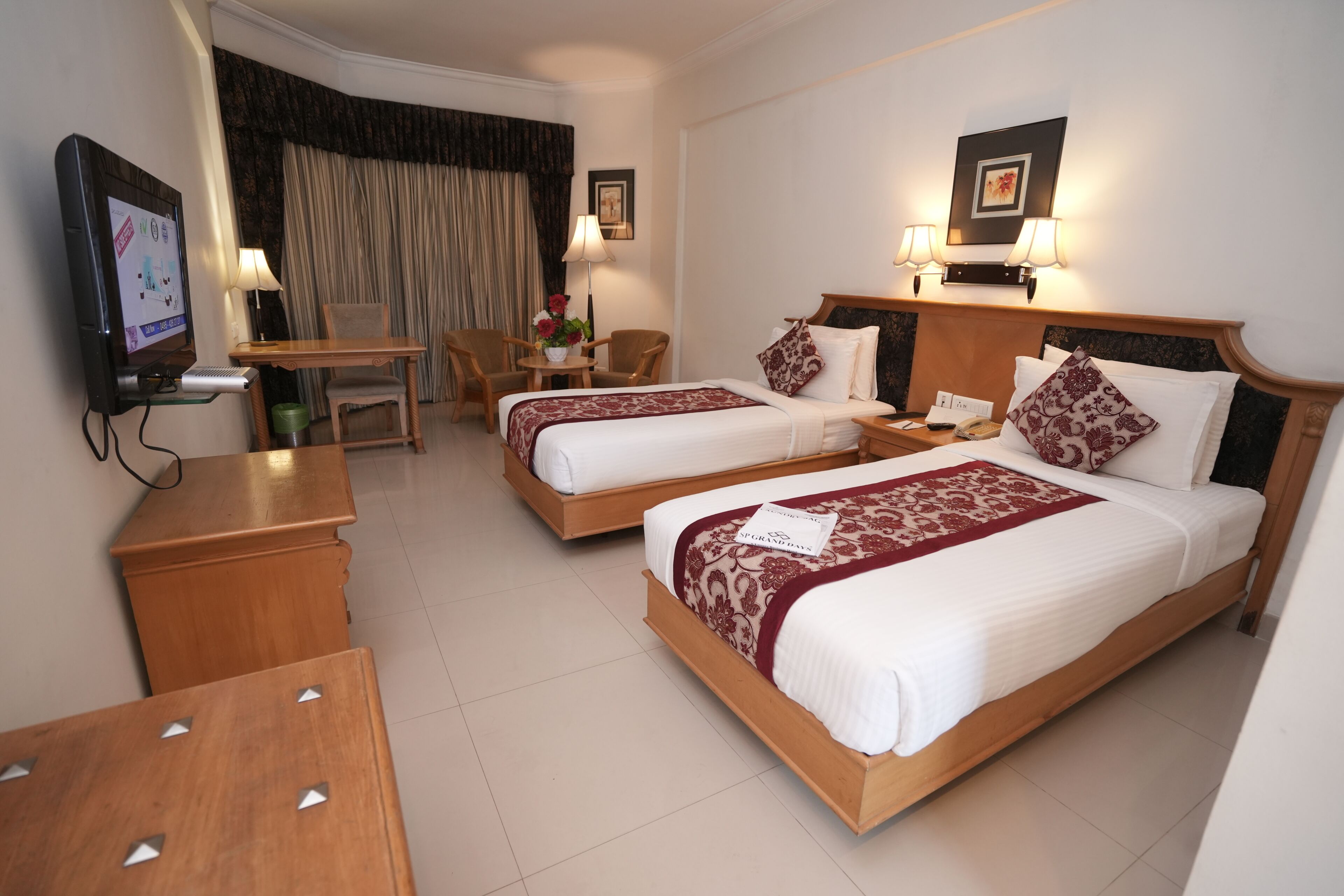 A hotel room with two beds, a TV, a desk, and a chair.