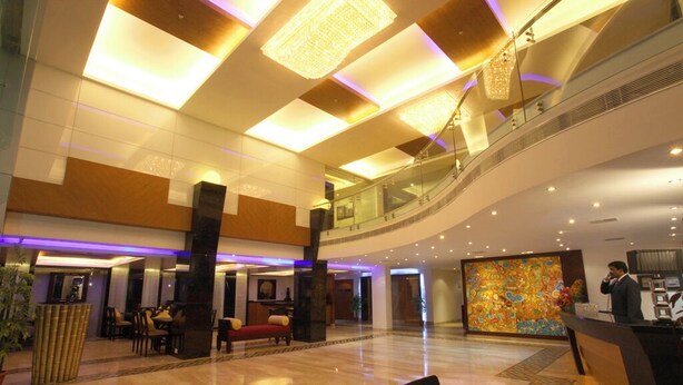 Een ruime lobby met een hoge plafond, een glazen trap en een receptiebalie.