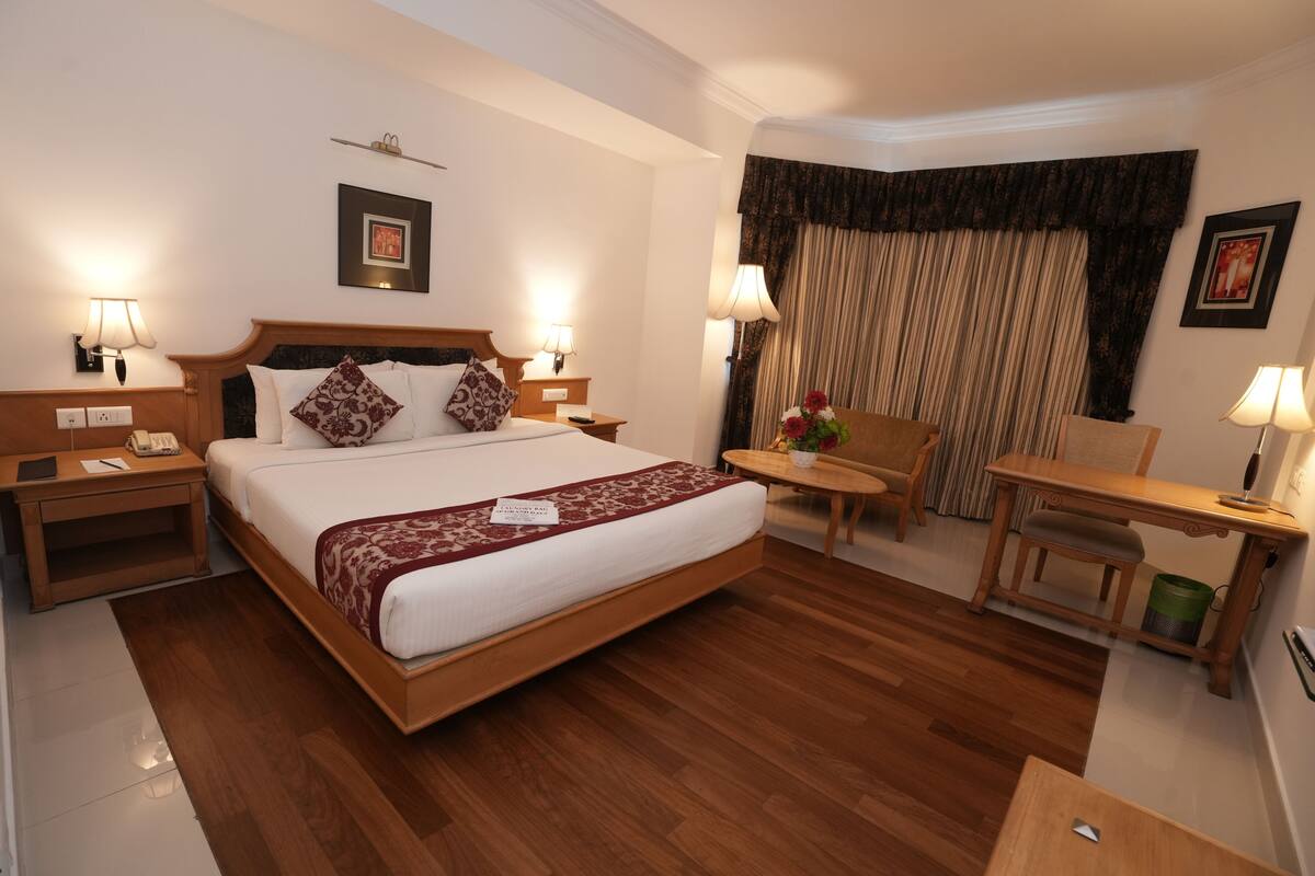 A hotel room with a large bed, bedside tables, a desk, a chair, and a small table with a vase of flowers.