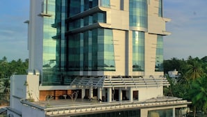Een meerlaags hotel met een moderne glazen gevel, een terras op het dak en een parkeerplaats met verschillende auto's.