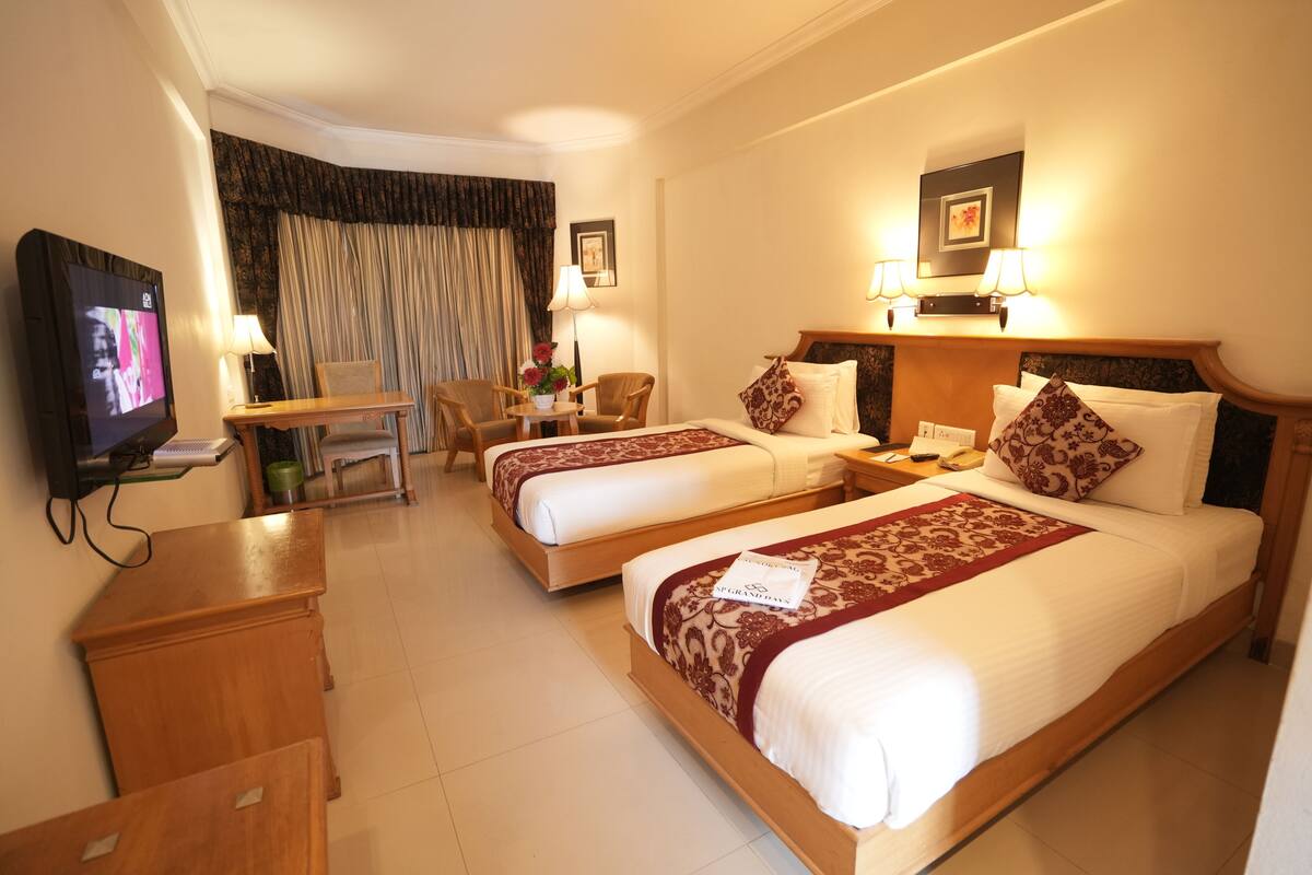 A hotel room with two beds, a desk, a television, and a chair.