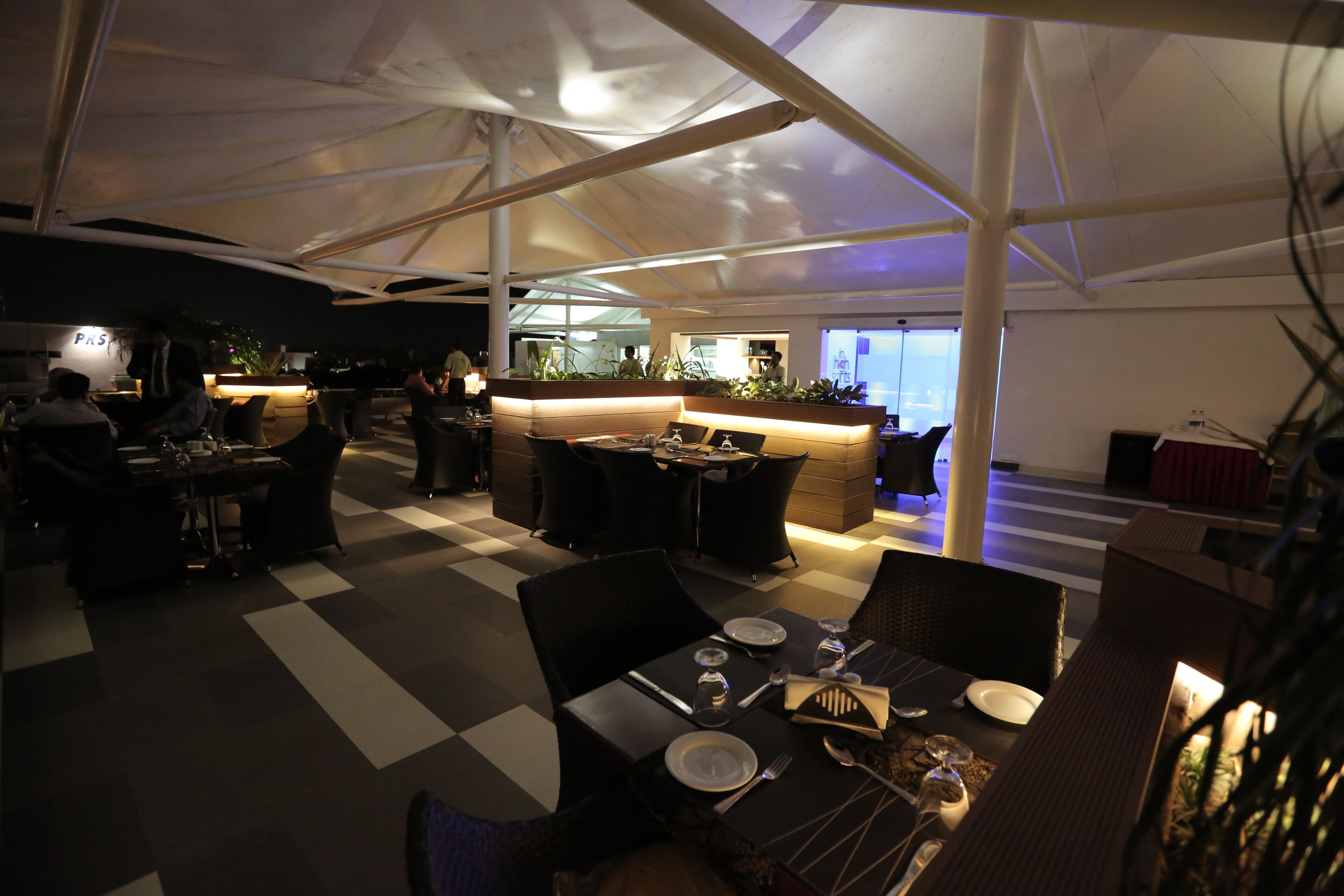Un restaurant avec un sol à carreaux, des chaises noires et blanches et un coin bar agrémenté de plantes.