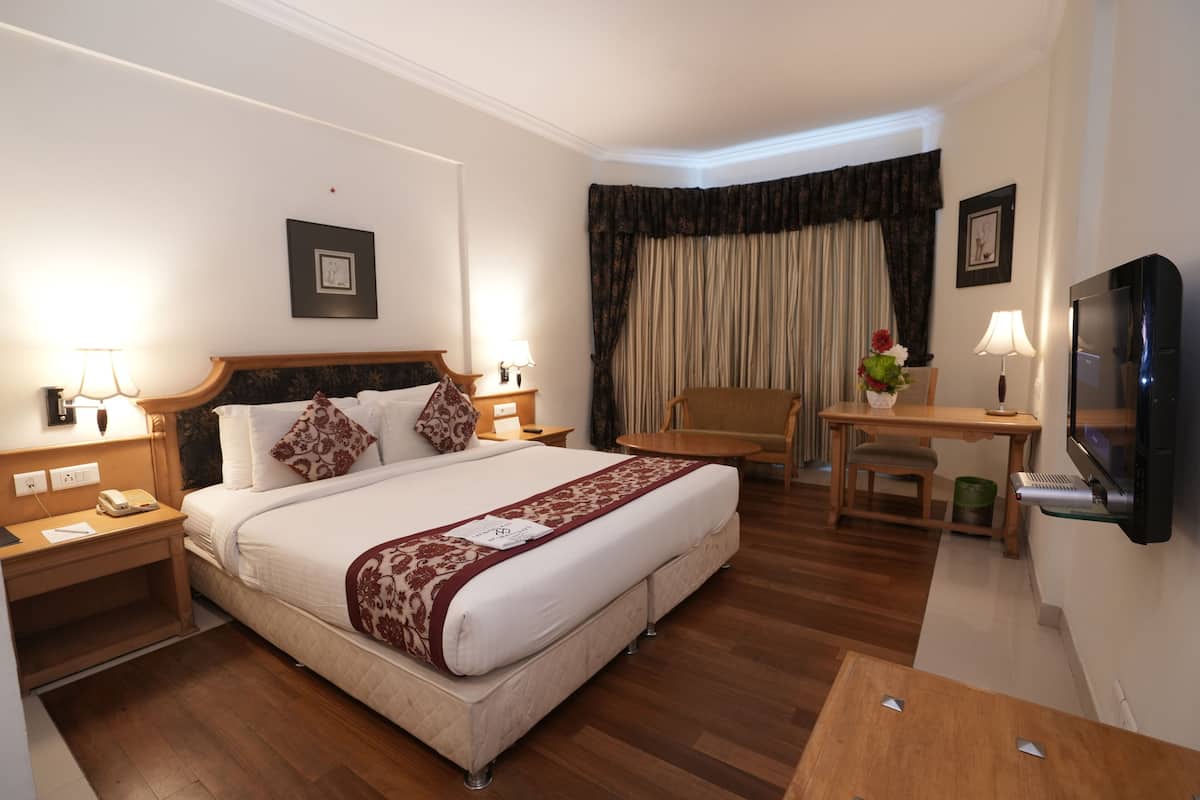 A hotel room with a large bed, bedside tables, a desk, a chair, a TV, and a window with curtains.