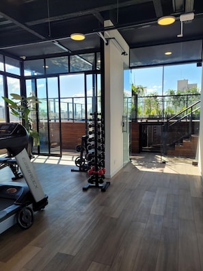 A gym with exercise equipment, large windows, and a view of buildings outside. - Bewiki (Florianópolis)