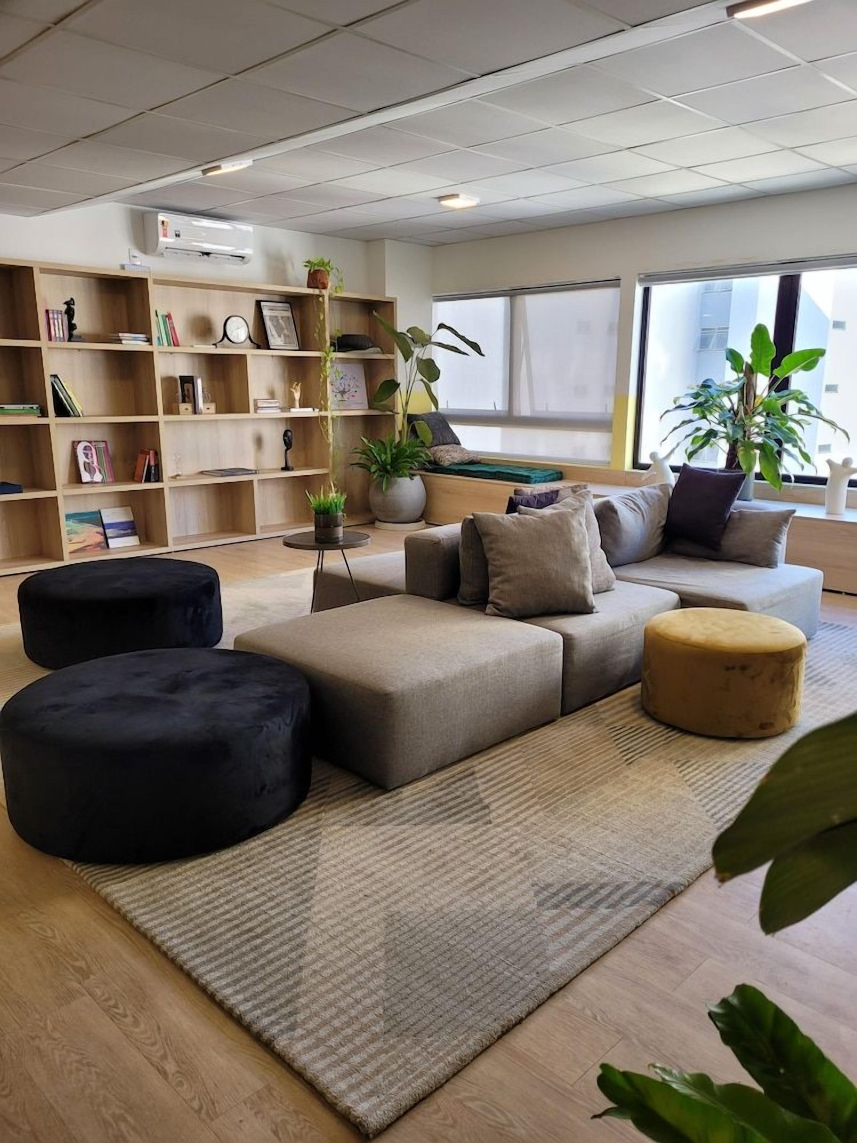 Un salon moderne avec un canapé d’angle, des poufs noirs et beige, une bibliothèque et des plantes en pot.