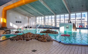 Sisätiloissa sijaitseva uima-allas, jossa on kirkasta vettä, kallioita ja aurinkotuoleja.