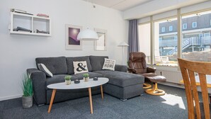 A modern living room with a grey sofa, a round coffee table, a brown leather chair, and a window with a view of buildings. - Sondervig Holiday Center (Ringkobing)